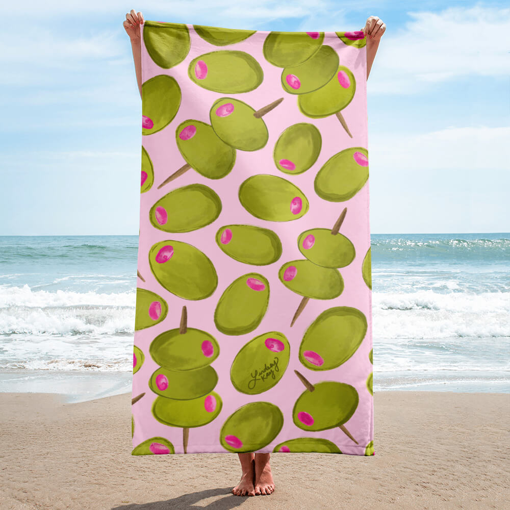 Hand-illustrated green olive pattern beach towel on pink background by Lindsey Kay Collective. Preppy pool towel for trendy girls, martini lovers, bachelorette party gifts, summer beach days, and aesthetic vacation essentials. 30x60 soft cotton polyester towel, perfect for poolside decor and olive-themed gifts.